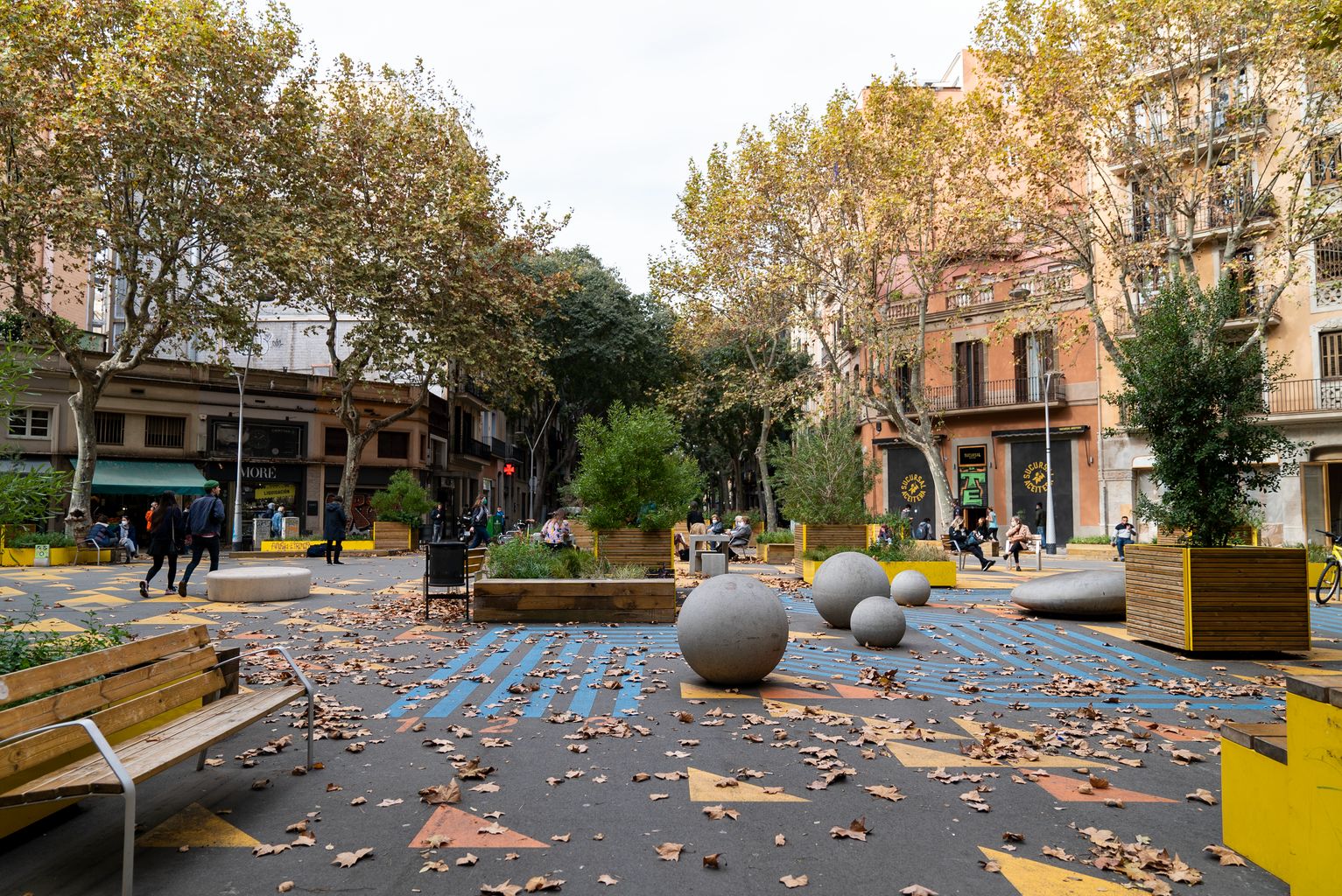 Vista d’una de la zones de la superilla de Sant Antoni amb jocs infantils dibuixats al terra, esferes de formigó, jardineres amb bancs i altre mobiliari urbà