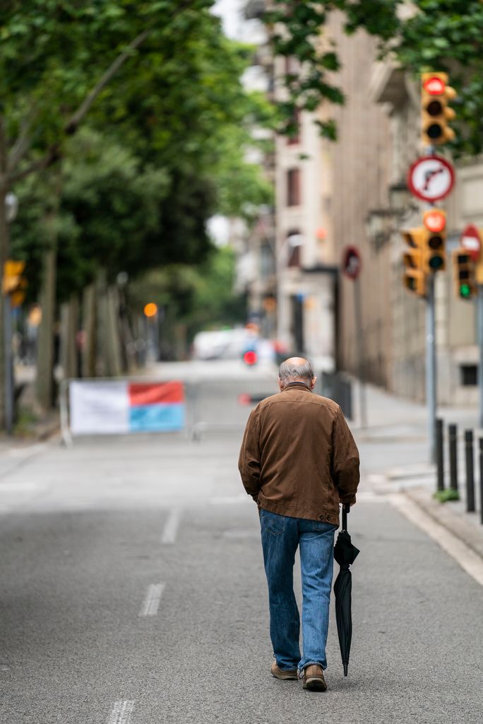 Home amb un paraigua a la mà caminant per les zones ampliades per a vianants de la xarxa d'itineraris segurs al lateral de l'avinguda Diagonal