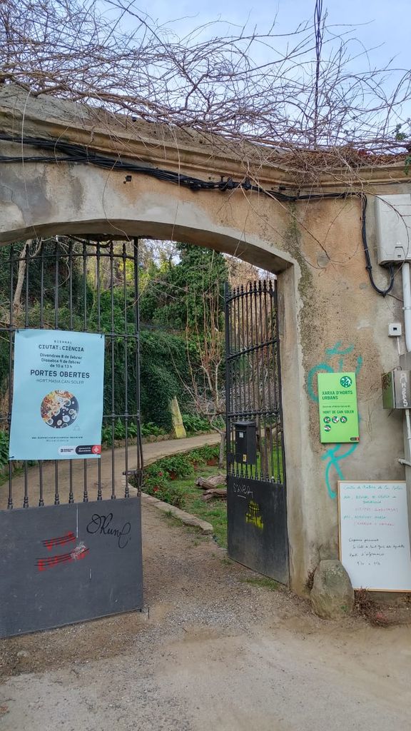 Porta d'entrada a l'hort amb el cartell de les portes obertes amb motiu de la Biennal Ciutat i Ciència