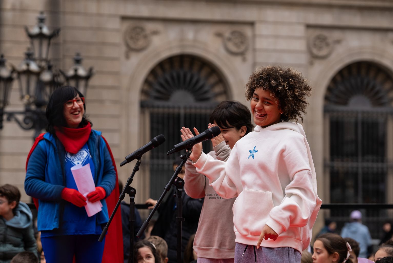 Dos niños delante de los micrófonos con Súper Laia durante la lectura del Pregón de los Niños y Niñas 2025