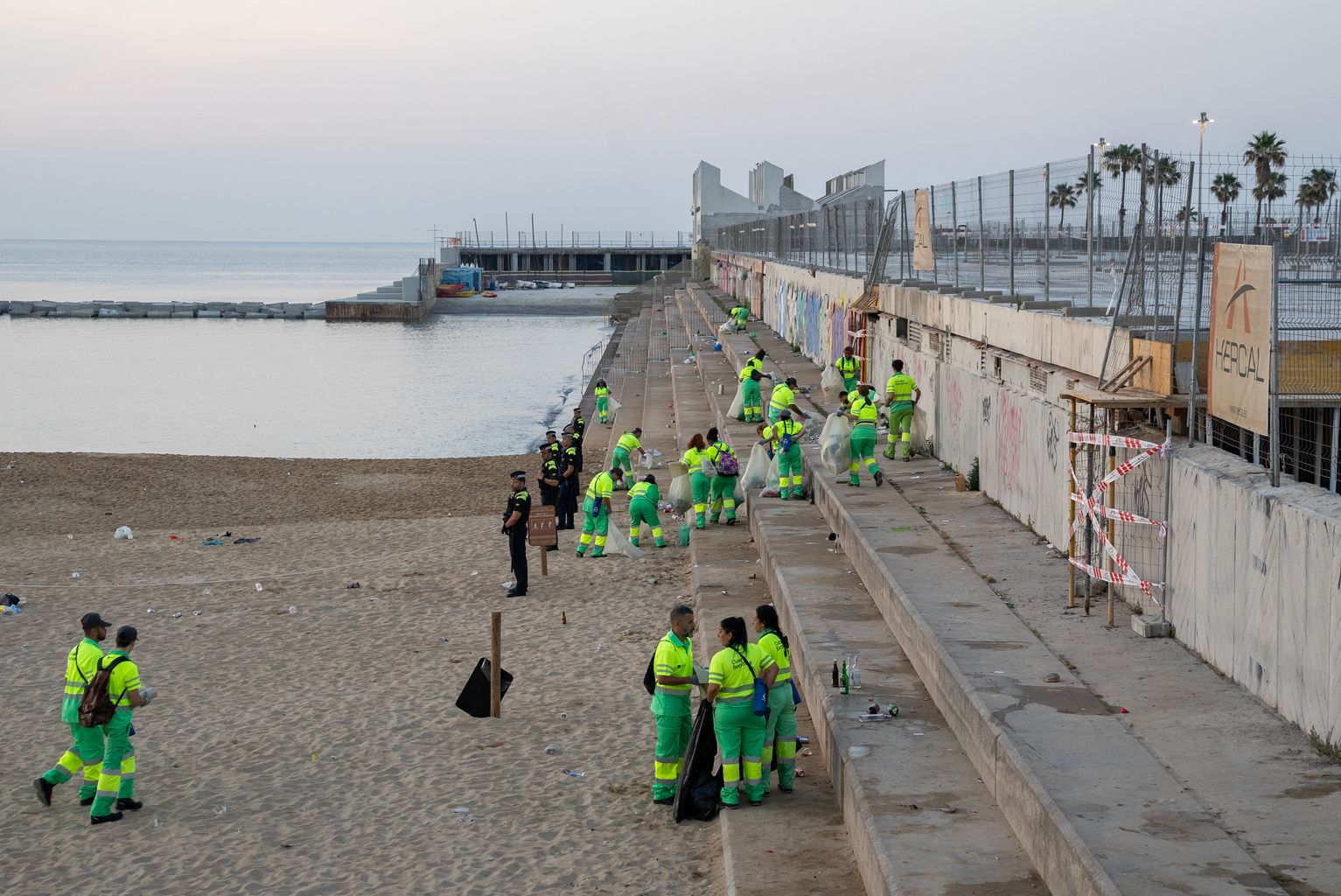 Diferentes operarios de limpieza recogiendo los residuos de las gradas de la playa de la Nova Icària después de la verbena de San Juan.
