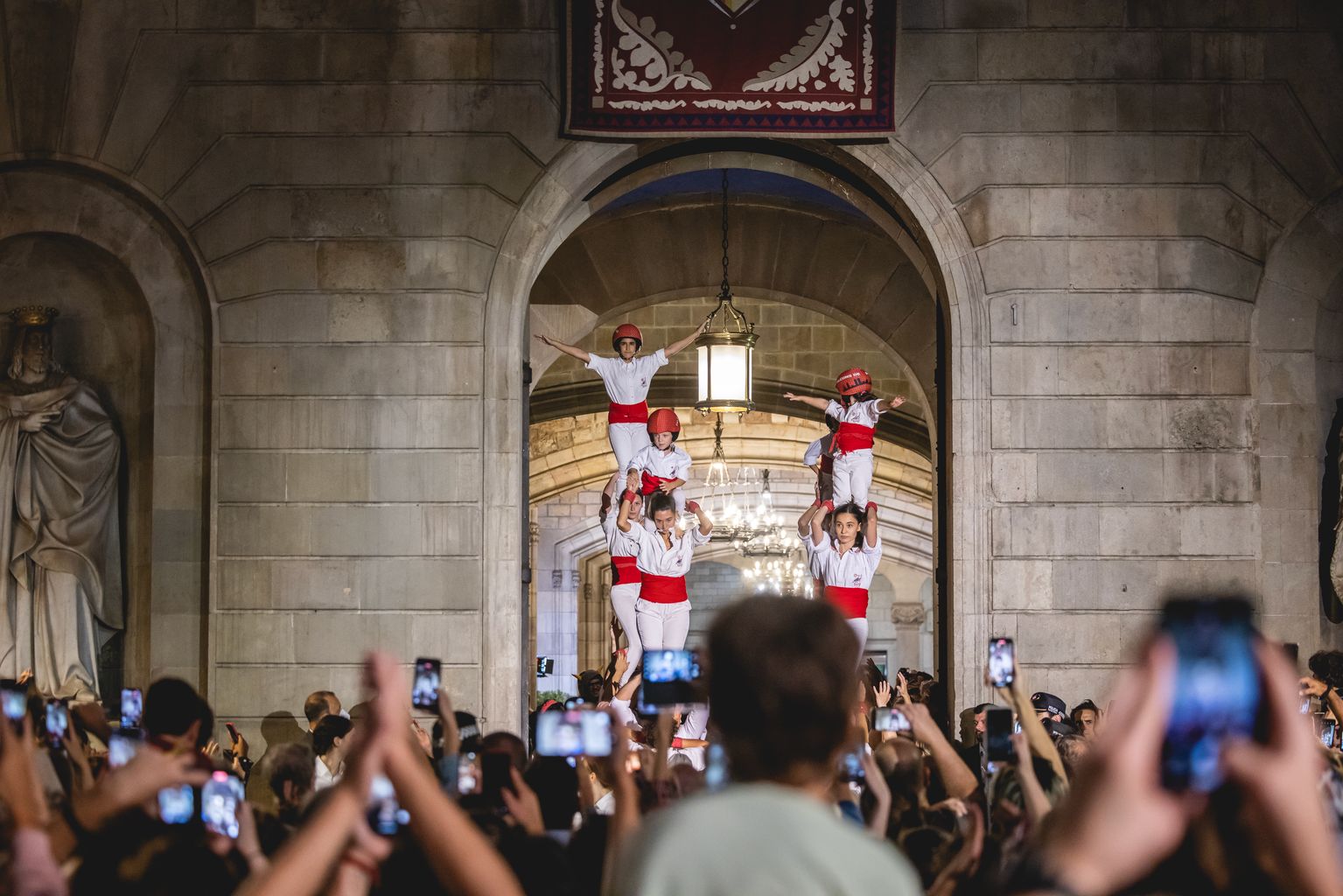 Falcons de Barcelona sortint fent pilars del pati de l’Ajuntament cap a la plaça de Sant Jaume durant el Toc d’Inici. A la plaça, molta gent aprofita per fotografiar el moment