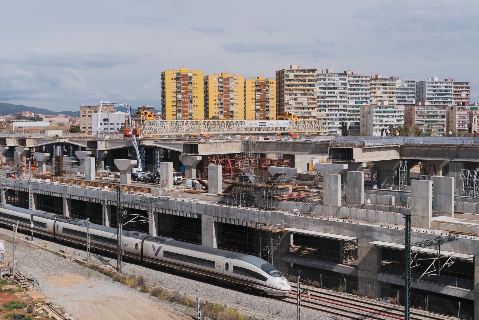 Vista general de les obres de la Sagrera. Hi circula un tren. Al fons, edificis d'habitatges.