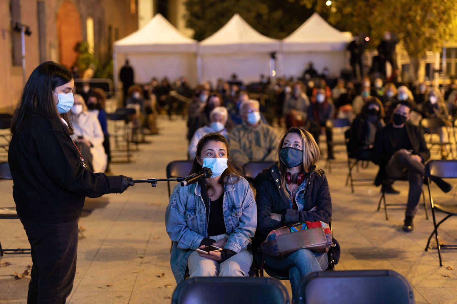 Taula rodona i performance "Mirar el futur". Una dona del públic fa una pregunta als ponents amb el micròfon que sosté a distància un membre de l'organització