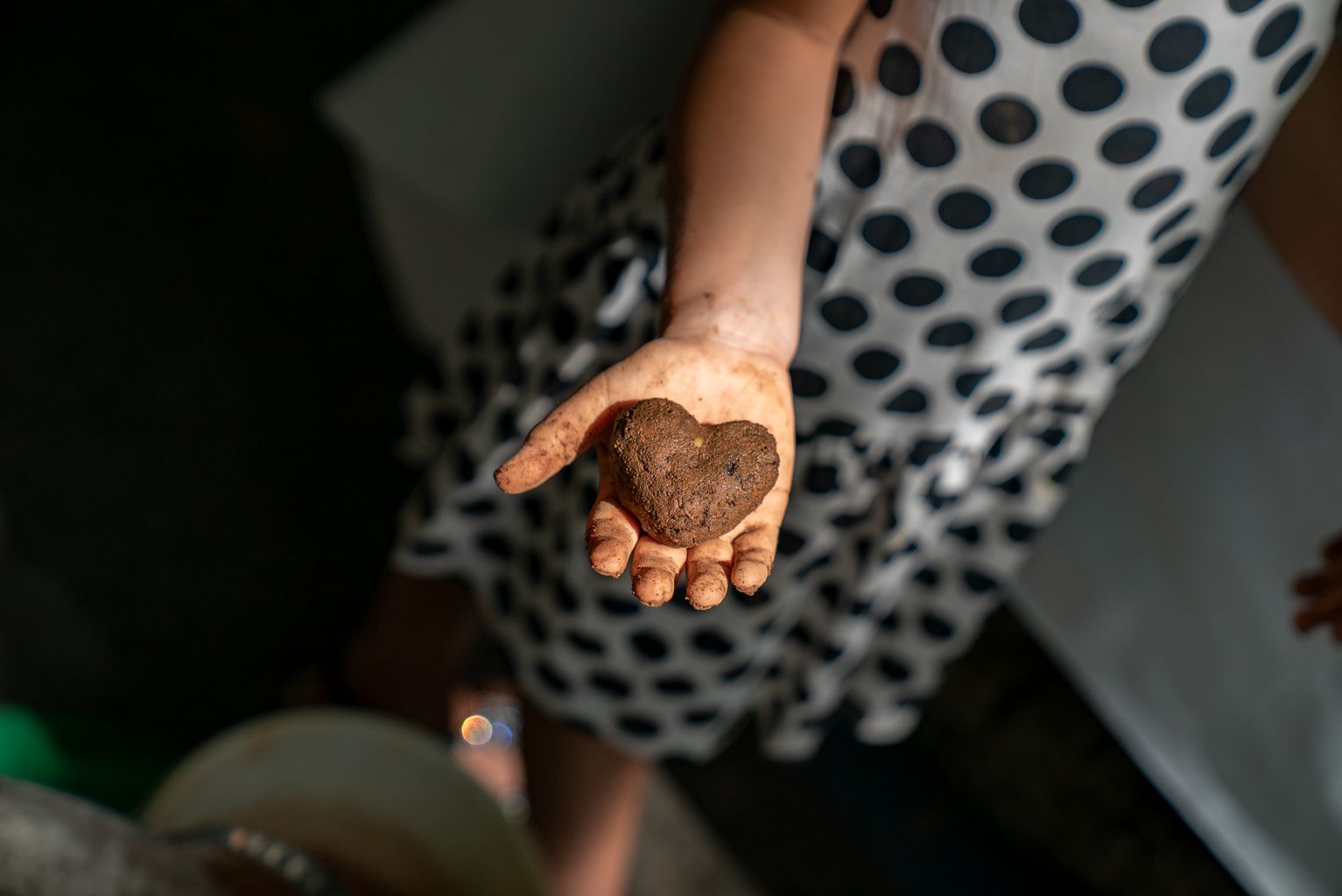 Una niña muestra un corazón hecho con barro, abono y una mezcla de semillas de plantas aromáticas y comestibles realizada en el taller “Hacemos bolitas de semillas: nenodango”, de la Fiesta Mayor de Gràcia