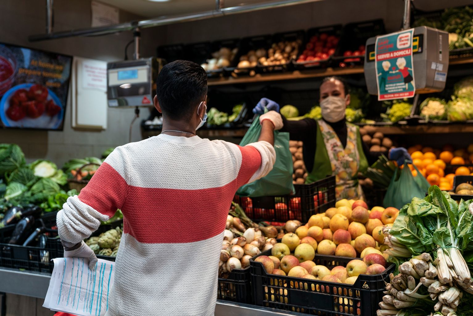 Uno de los repartidores del servicio a domicilio del Mercado de Sant Antoni recoge un pedido en un puesto de frutas y verduras