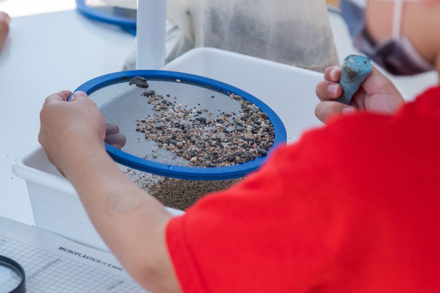 Un infant mira amb una lupa els microplàstics que es poden trobar en una mostra de sorra del mar durant l’activitat “Descobrim els microplàstics!”, de la Festa de la Ciència