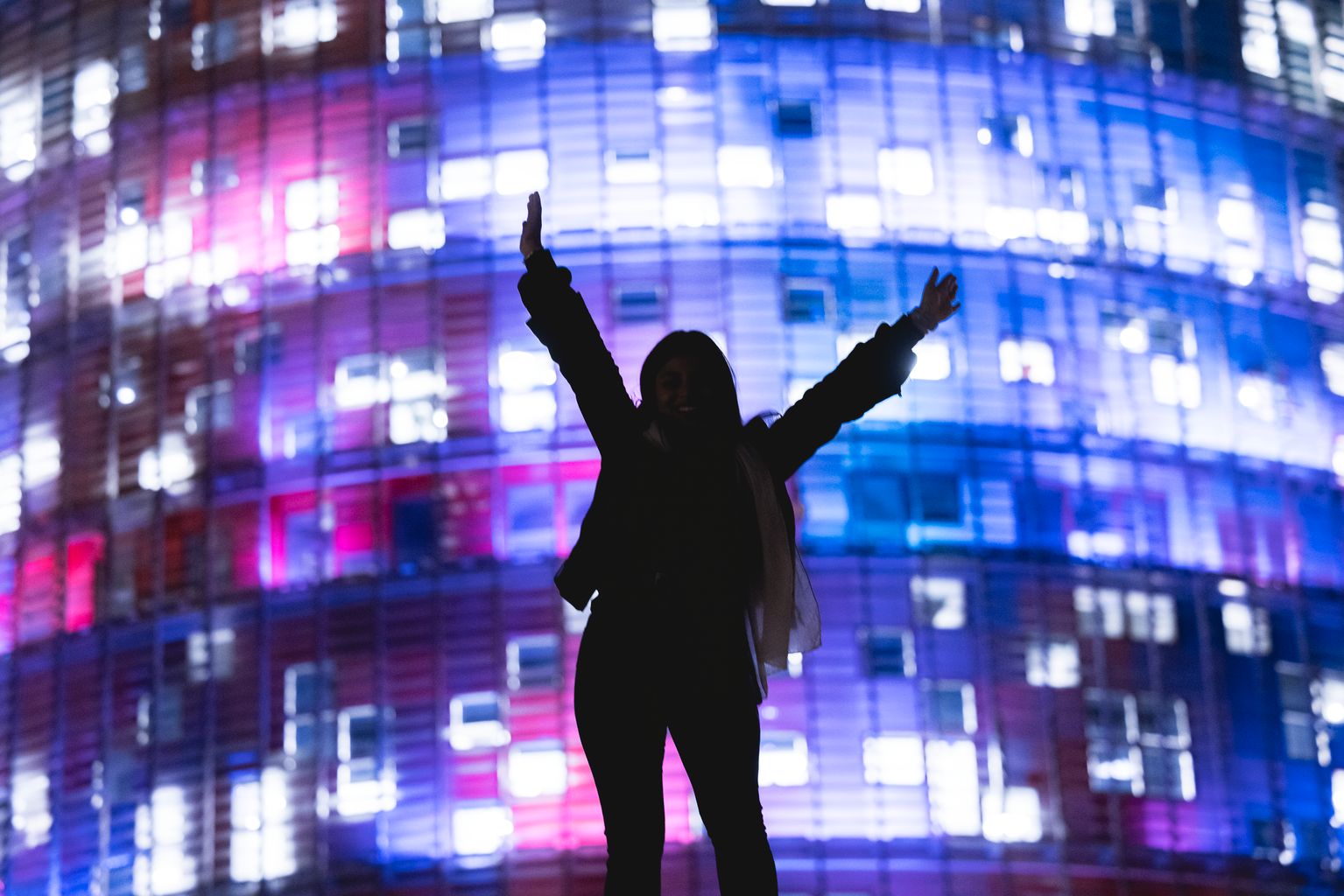 Una dona posa davant de la Torre Glòries il·luminada amb motiu del LlumbBCN