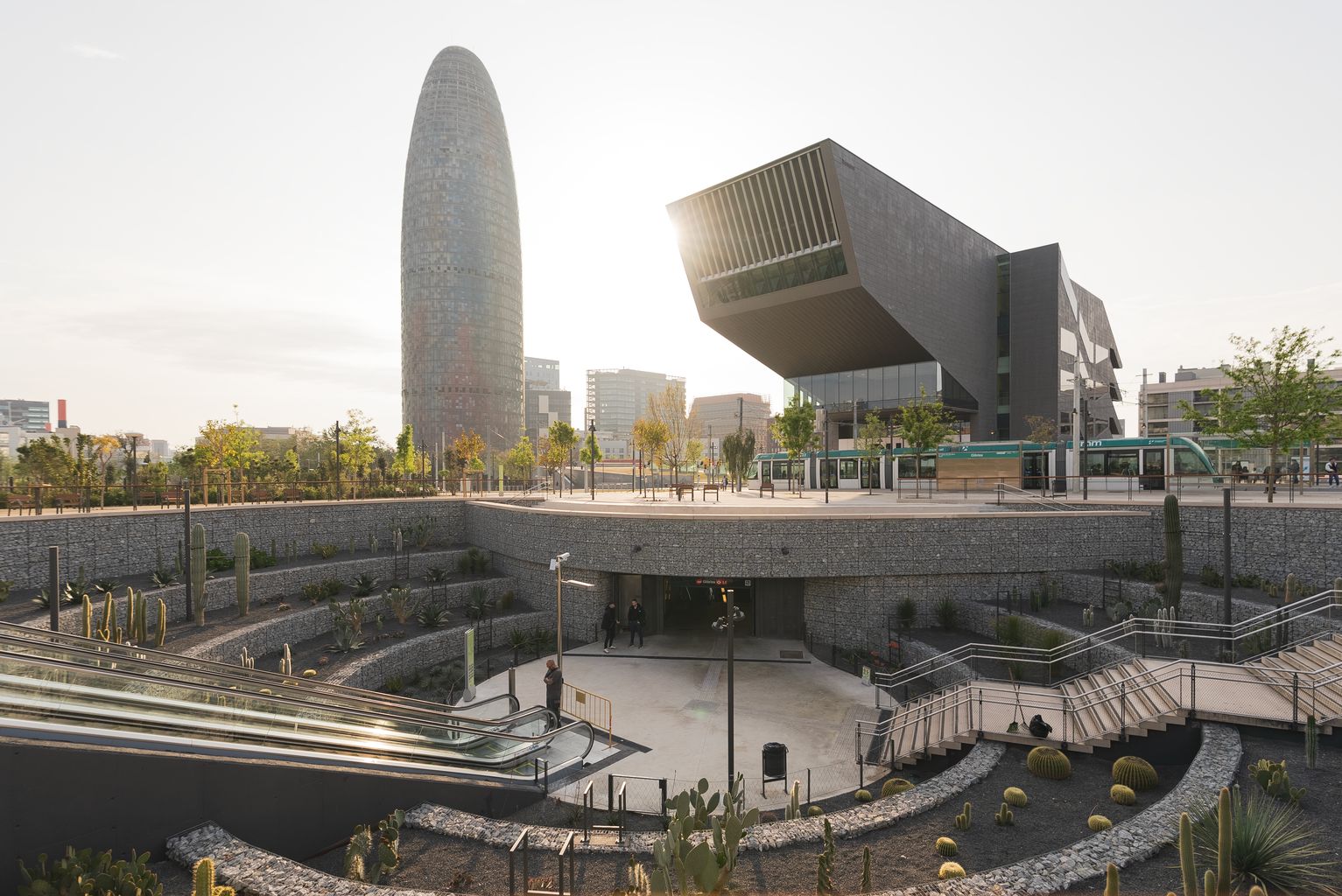 Zona del nou parc de les Glòries amb un jardí d'immersió que dona accés al metro amb una graderia de mirador i de fons el Museu del Disseny de Barcelona (DHub Barcelona) i la Torre Glòries