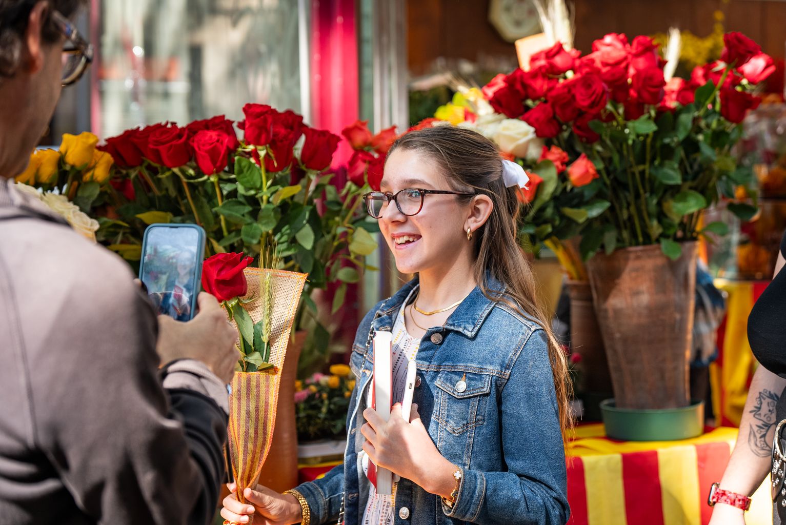 Una nena amb una rosa i un llibre a la mà mentre li fan una fotografia el dia de Sant Jordi