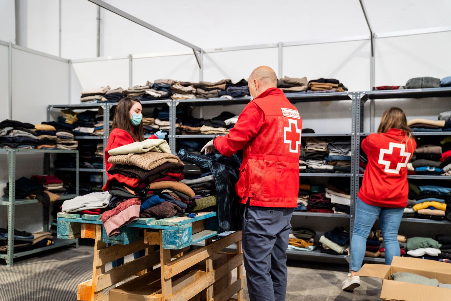 Miembros de la Cruz Roja organizan la ropa y los zapatos que les han llegado al pabellón para personas sin hogar