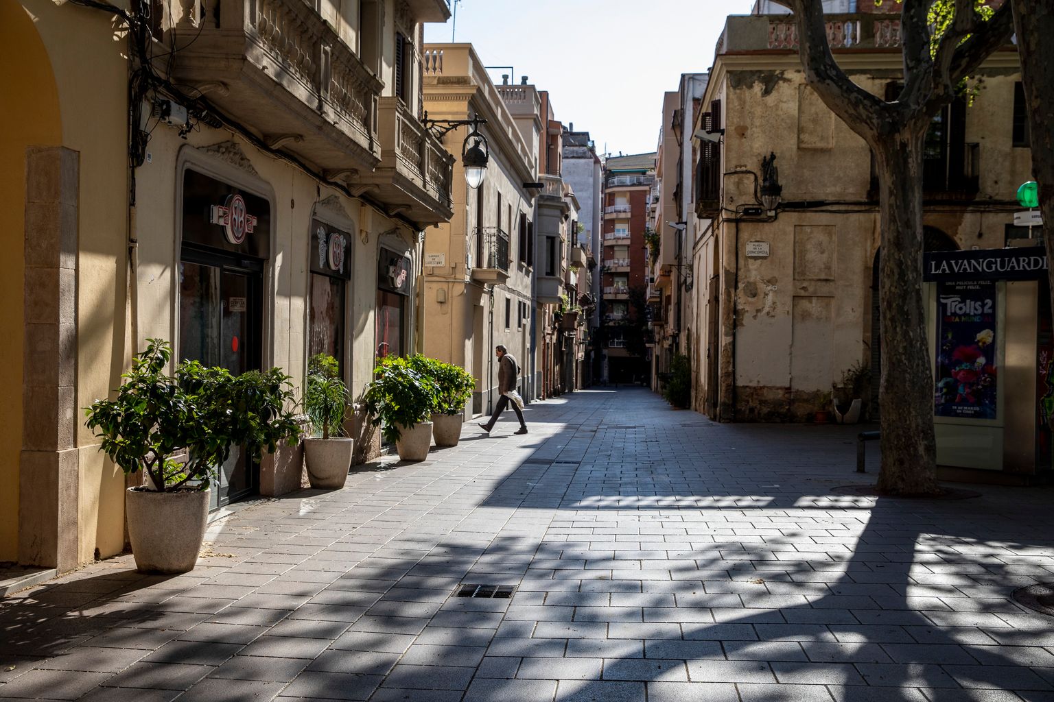 Plaça de la Concòrdia per on passa un home carregat de bosses. Districte de les Corts.