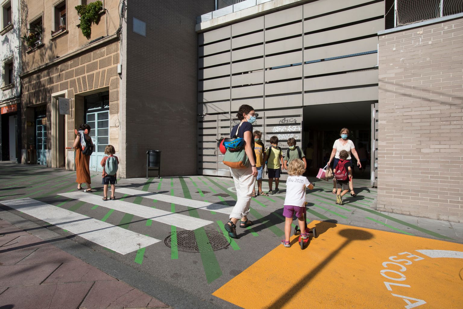 Una dona amb el nen creuen pel pas de vianants de la zona pacificada davant de l’Escola l’Univers. Es veu la senyalització horitzontal pintada a la calçada que avisa de la proximitat d’una escola