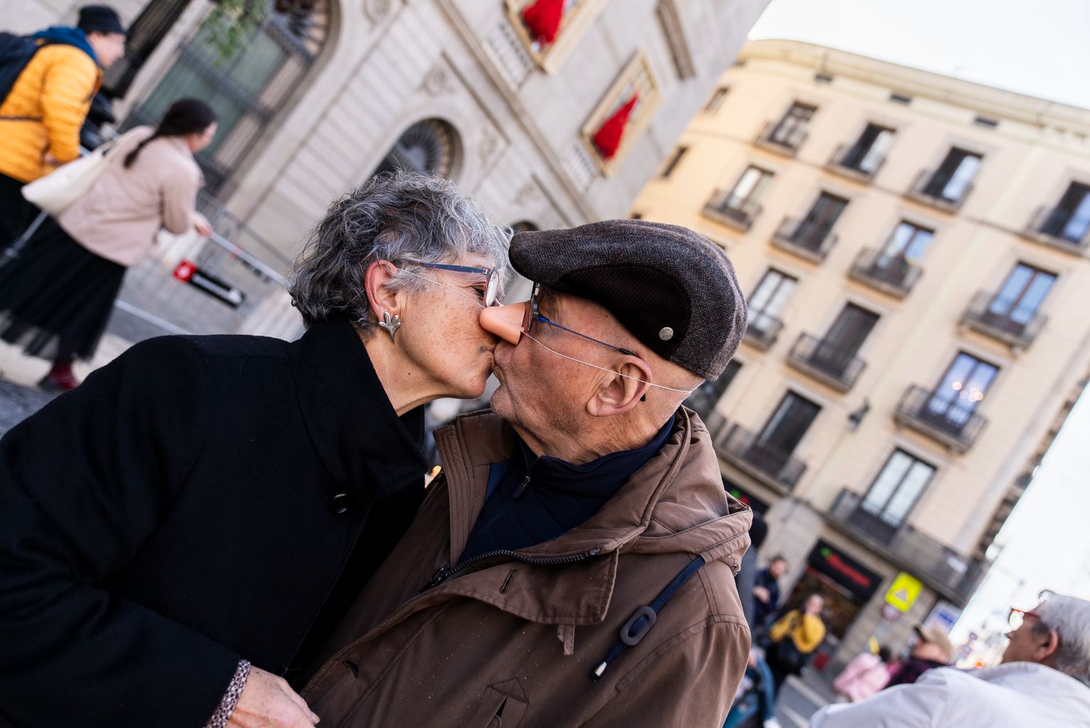 Dos assistents a la cercavila de l’Home dels Nassos es fan un petó amb dos nassos característics a la plaça de Sant Jaume