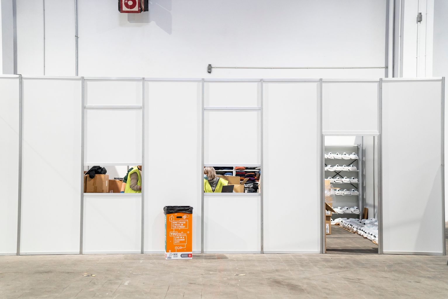 Pavelló per a persones sense llar. Punt d’atenció i de repartiment de roba, sabates i roba blanca (tovalloles) amb dues finestretes per atendre les persones. Dins hi ha diversos treballadors enllestint la feina