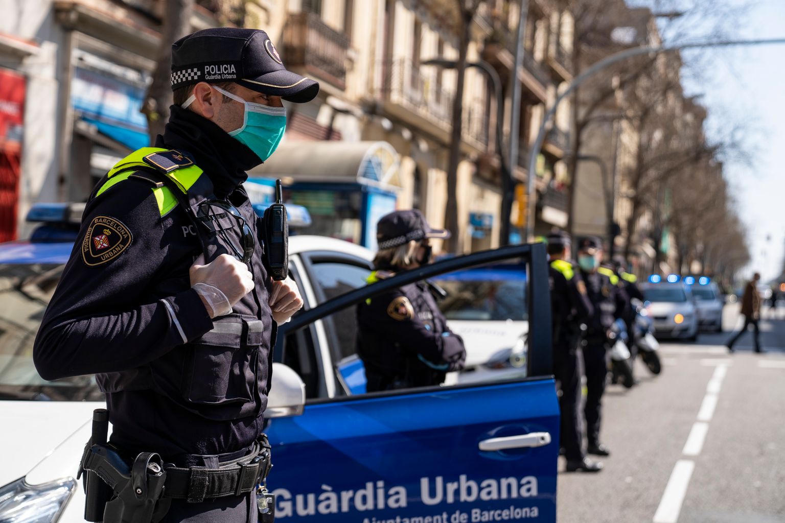 Cotxes i agents de la Guàrdia Urbana amb mascaretes i guants parats davant del Mercat d'Hostafrancs per retre l'homenatge als treballadors dels Mercats Municipals