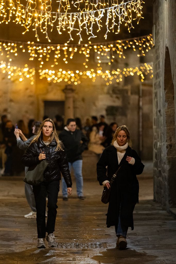 Dos chicas pasean bajo las luces de Navidad de la calle de Sant Felip Neri, con el oratorio al fondo