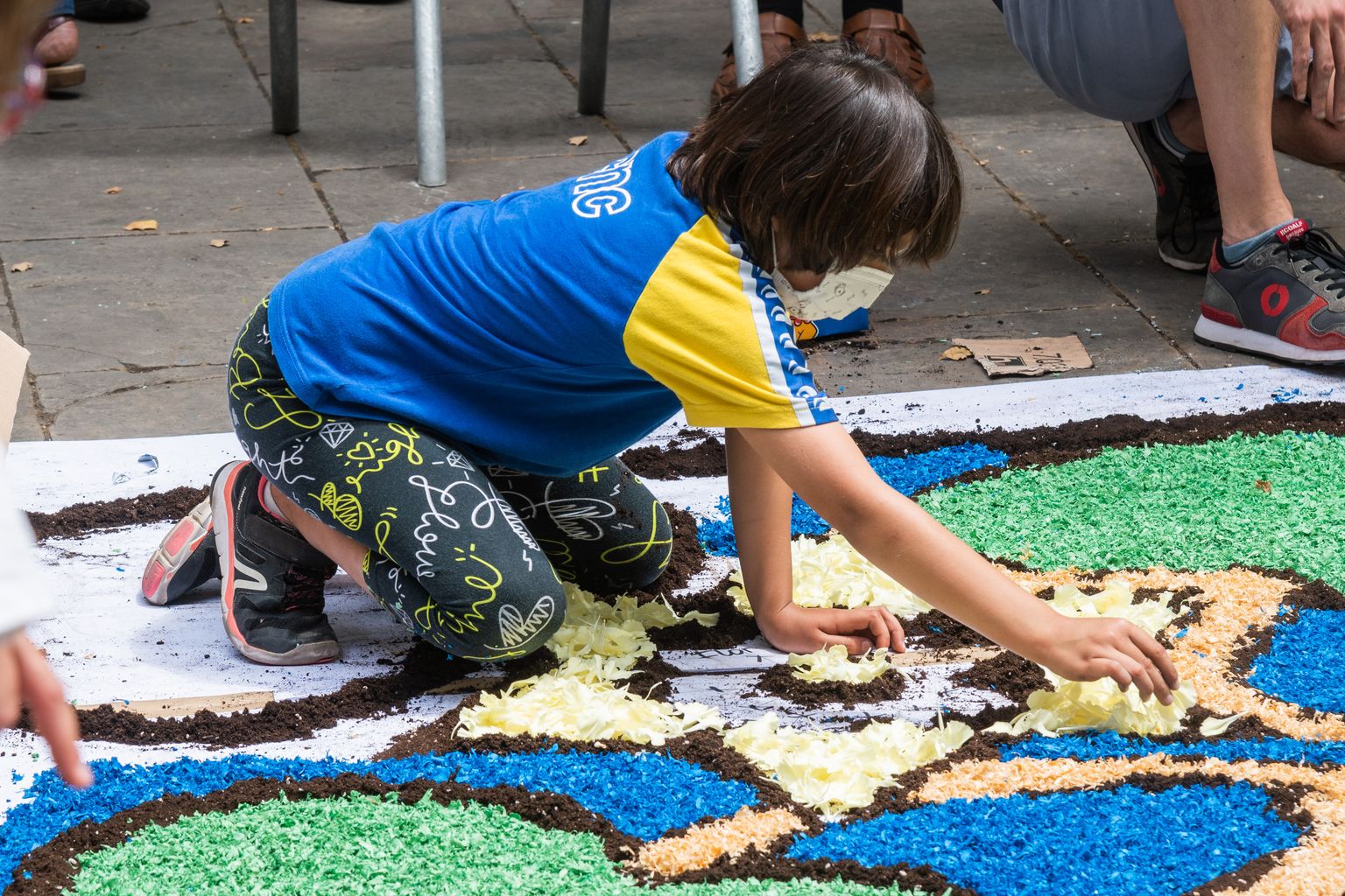 Un niño va colocando flores en la alfombra floral de la plaza de la Virreina, elaborada con motivo de la fiesta del Corpus