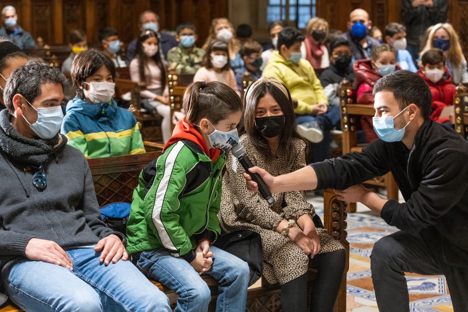 Un nen recita el seu fragment del Pregó dels Infants de les Festes de Santa Eulàlia al Saló de Cent mentre un home sosté el micròfon.