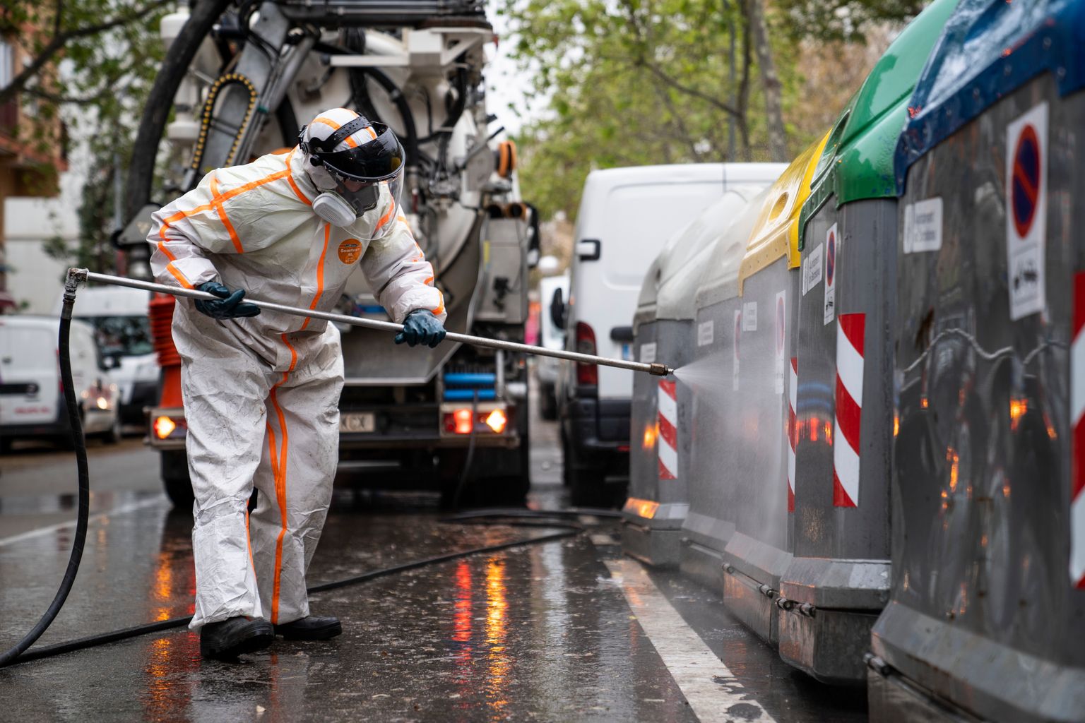 Un operari d’una empresa de serveis de neteja opera una llança d’aigua a pressió per desinfectar els contenidors