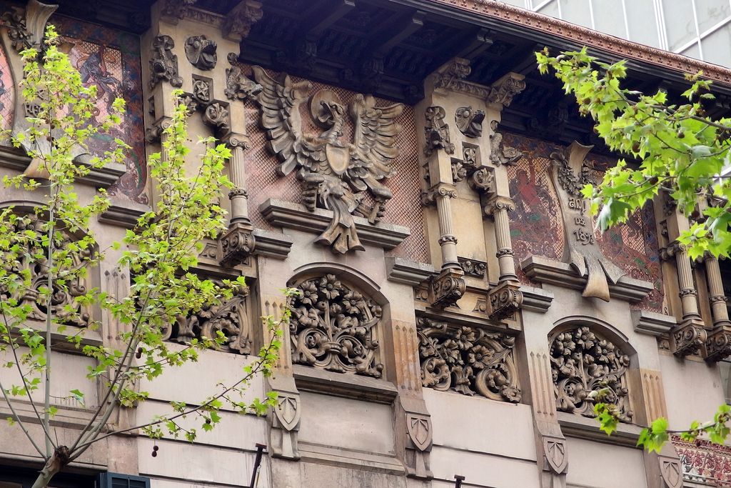 Palau Montaner. Detall del fris sota el ràfec amb una àliga de pedra i, al costat, hi ha mosaics i les dates de construcció de l'edifici