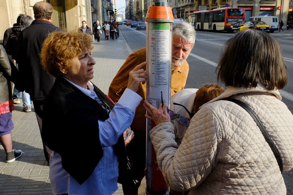 Persones consultant la informació de les rutes a la parada d'autobús a la via Laietana