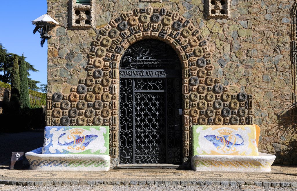 Torre Bellesguard - Casa Figueres. Façana de pedra picada amb la porta principal amb arcada de pedra i reixa de ferro i bancs de pedra decorats amb mosaics