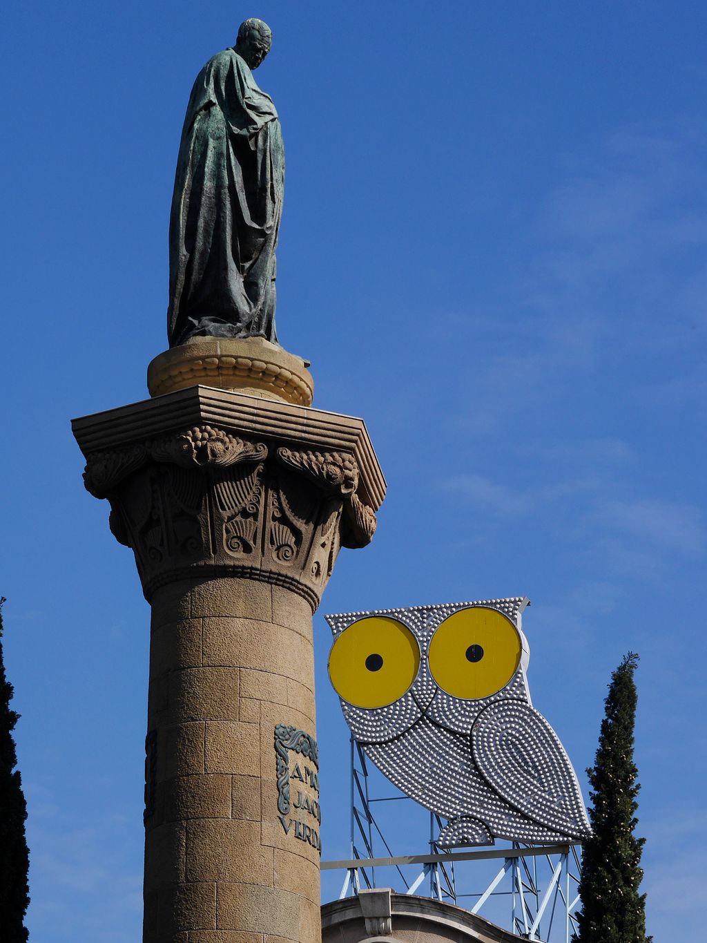 Rètol lluminós d'El Mussol a la plaça de Mossèn Jacint Verdaguer. Mossèn Cinto Verdaguer (escultura) i rètol