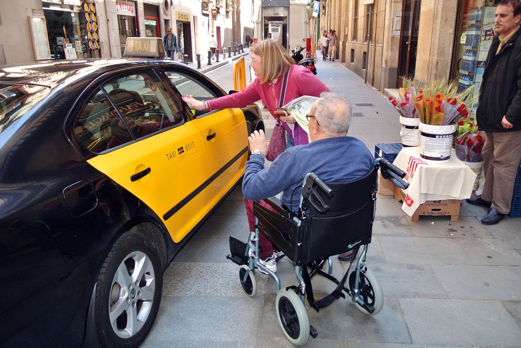 Home gran en cadira de rodes agafant un taxi