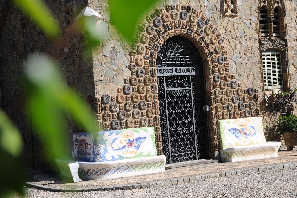 Torre Bellesguard - Casa Figueres. Porta principal amb arcada de pedra i reixa de ferro i bancs de pedra decorats amb mosaics