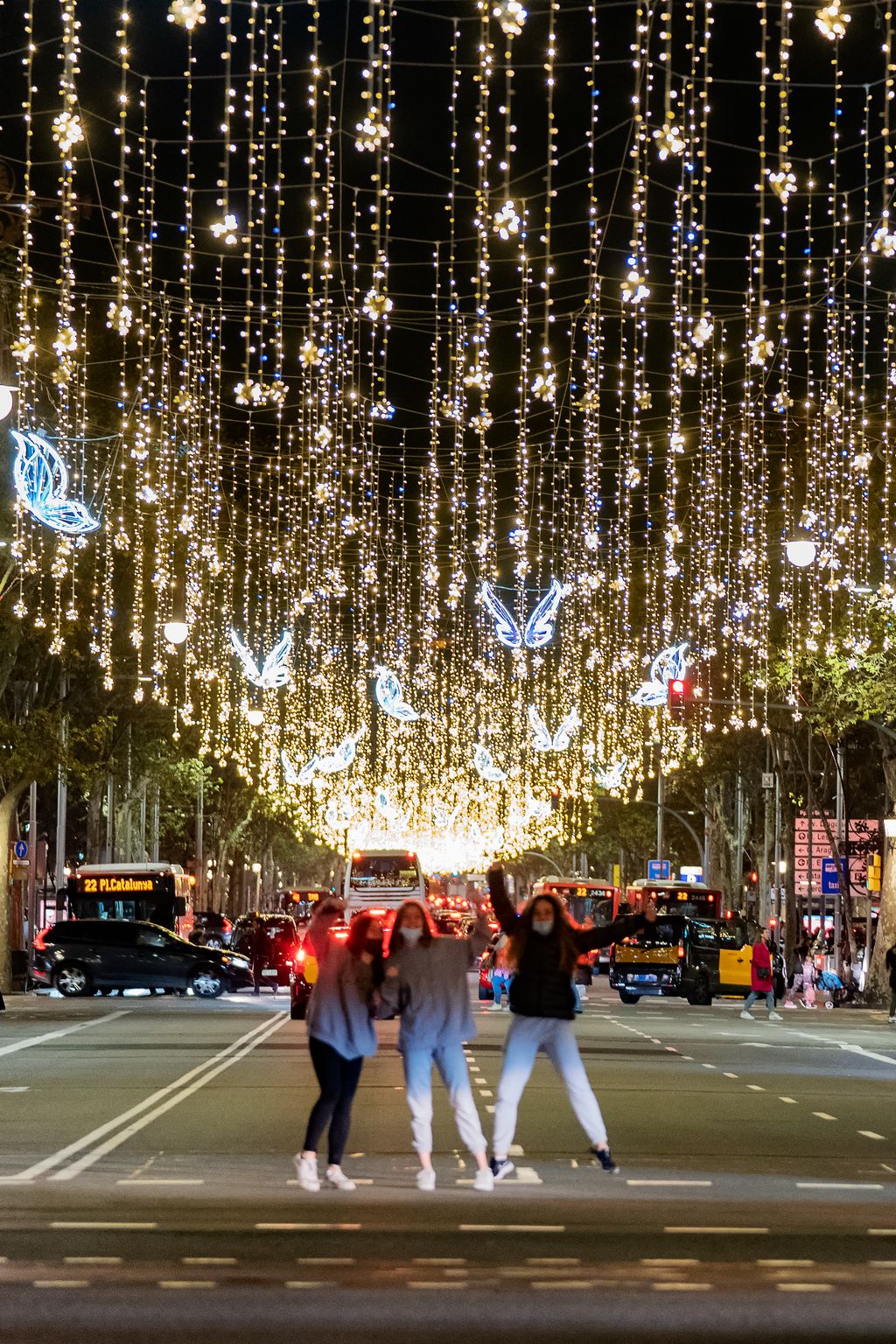 Unes noies es fan una selfie amb el fons dels llums de Nadal del passeig de Gràcia mentre creuen per un pas de vianants