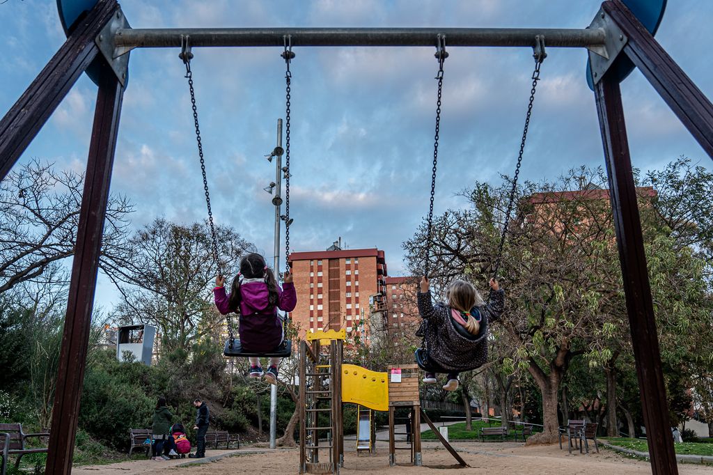 Unos niños se balancean en un área de juego infantil en el parque de Josep M. Serra Martí