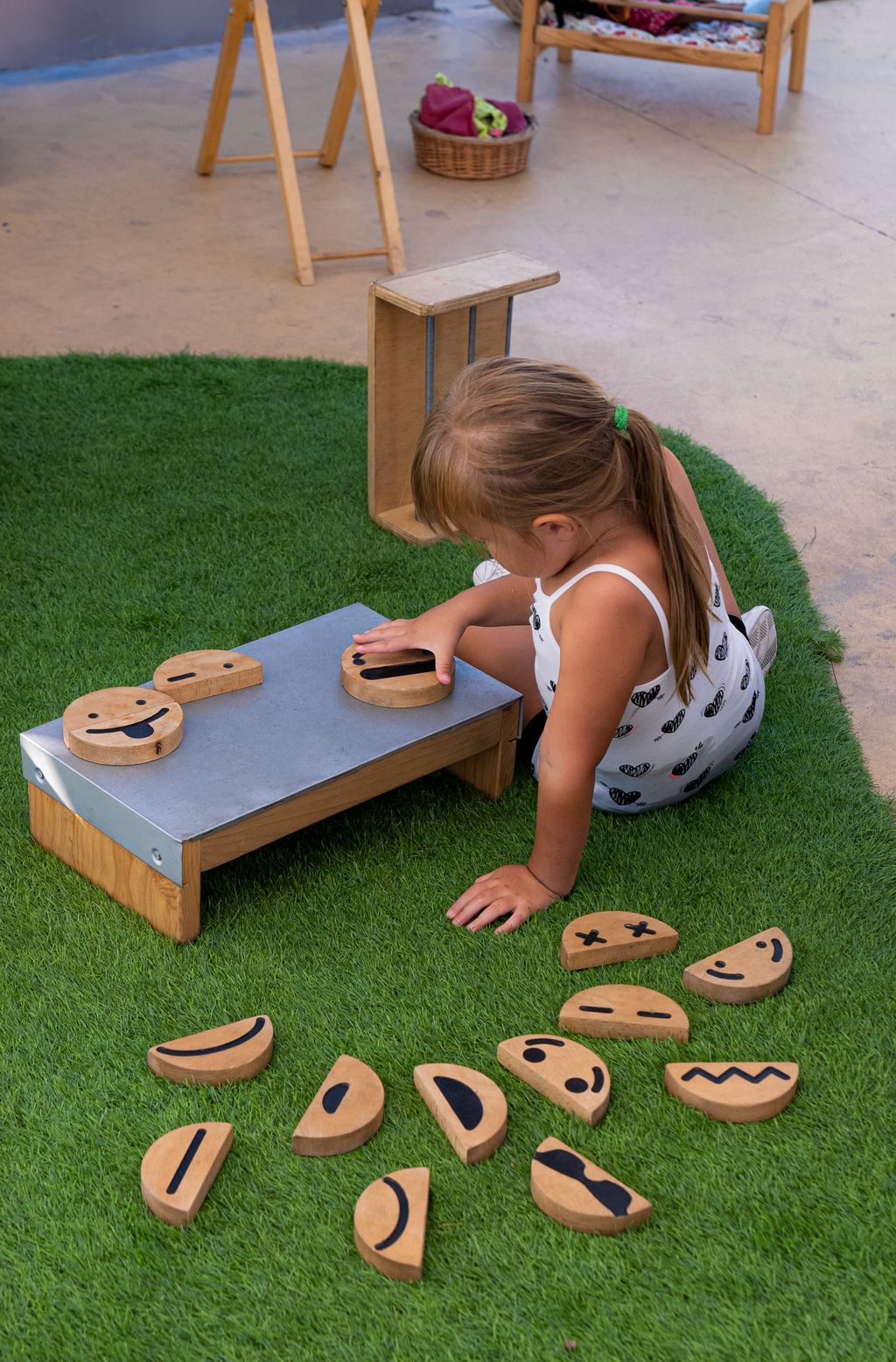 Una nena col·loca peces de fusta sobre una taula metàl·lica als Jardins de la Rambla de Santa