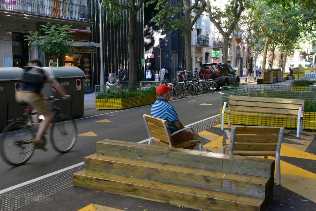 Home assegut a la zona pacificada del carrer del Comte Borrell (entre Parlament i Manso). Les voreres han estat ampliades sobre la calçada i estan separades pel carril de circulació per unes bandes rugoses i per mobiliari tàctic com bancs i jardineres
