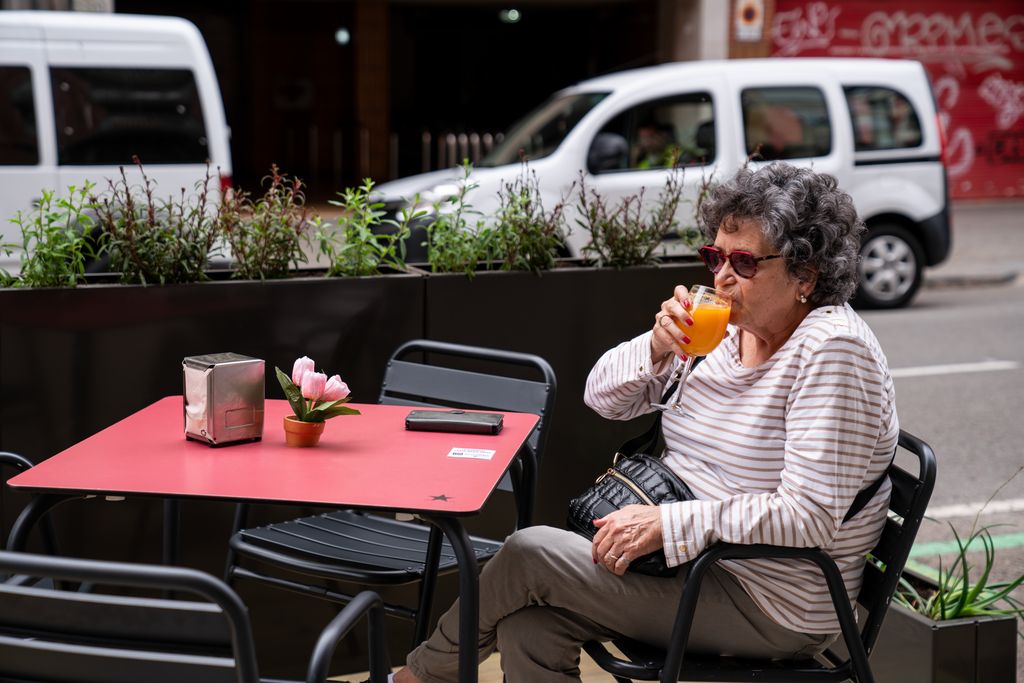 Una dona pren un suc de taronja en una cafeteria on hi ha instal·lat un dels nous prototips de terrassa consistent en una plataforma de fusta i una barana separadora del trànsit amb jardineres