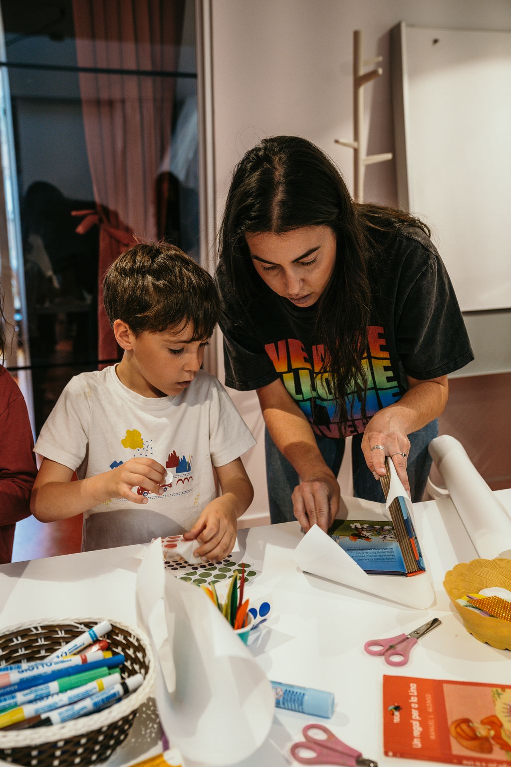 Una madre ayuda a su hijo a colocar un papel para hacer la funda para su libro de cuentos en uno de los talleres organizados con motivo de Sant Jordi.