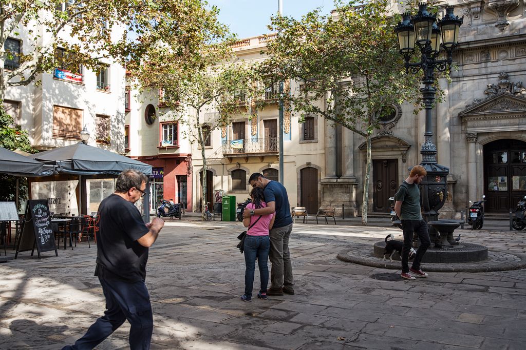 Personas paseando por la plaza de la Barceloneta con la fuente y la parroquia de Sant Miquel del Port