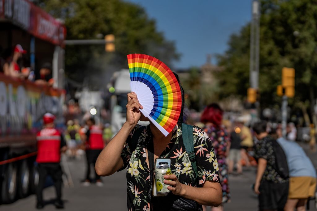 Una persona amb un ventall a la cara amb els colors de la bandera LGTBI durant la manifestació del Pride! 2023.