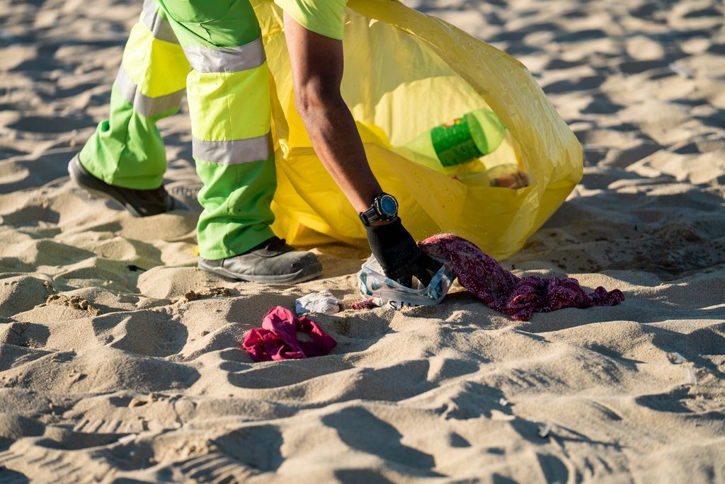 Un membre del Servei de Neteja de la ciutat recull una bossa de plàstic de la sorra de la platja del Bogatell que la gent ha deixat abandonada durant la celebració de la revetlla de Sant Joan