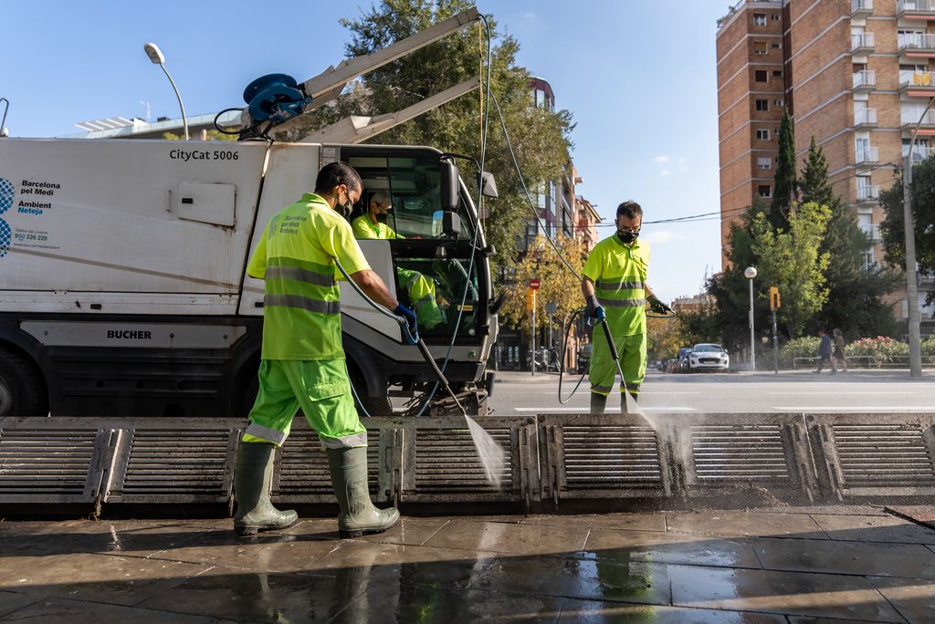 Unos trabajadores limpian con una lanza de agua a presión un imbornal recién vaciado y el pavimento de los alrededores con ayuda de un vehículo fregadora