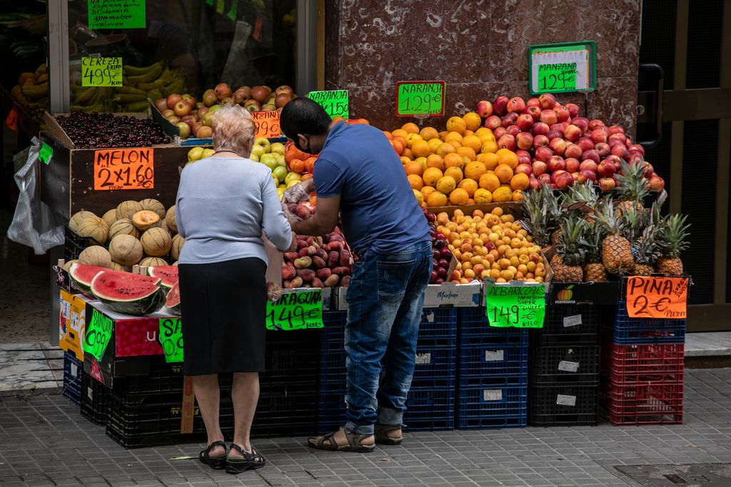 Un fruiter selecciona la fruita per a una clienta a l'exterior de la seva fruiteria a la via Júlia