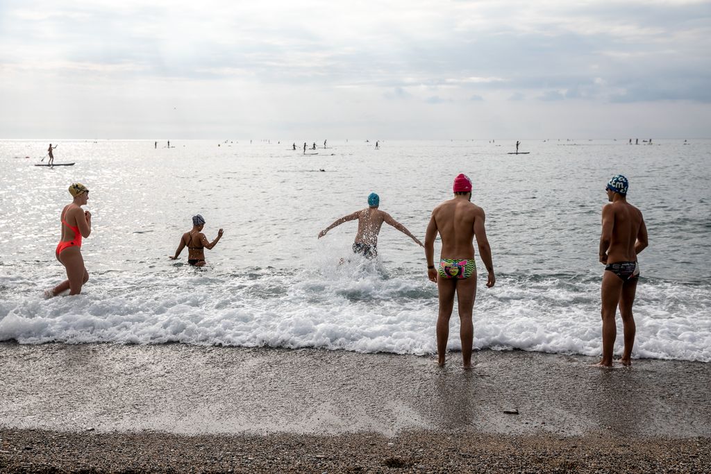 Nedadors entrant a l'aigua i, al fons, un grup de gent practicant surf de rem