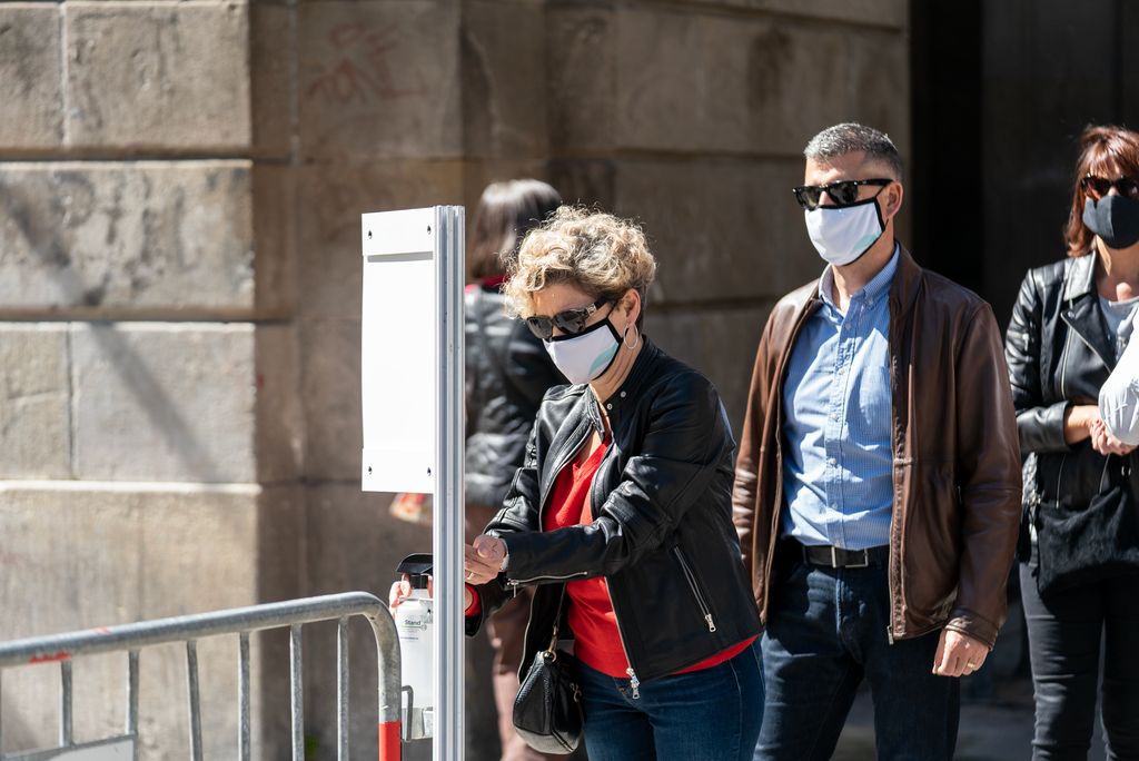 Gent fent cua i netejant-se les mans amb gel hidroalcohòlic per entrar al recinte firal de la plaça Reial, on es troba un dels recintes firals muntats amb motiu de Sant Jordi