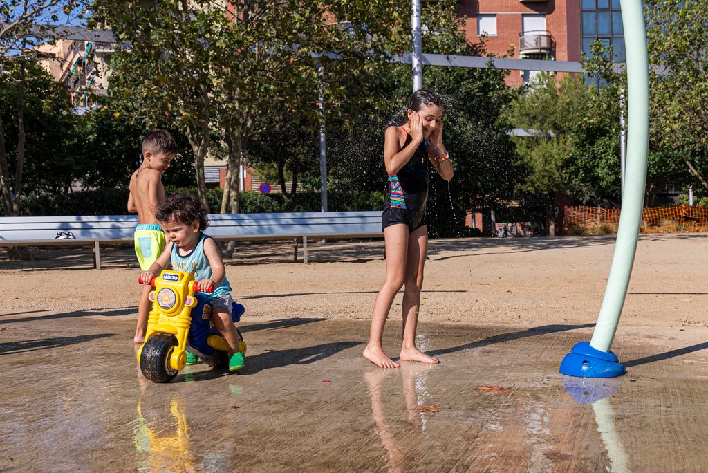 Un infants juguen a la zona d'aigua del parc de les Rieres d'Horta. Un nen va amb una moto de joguina