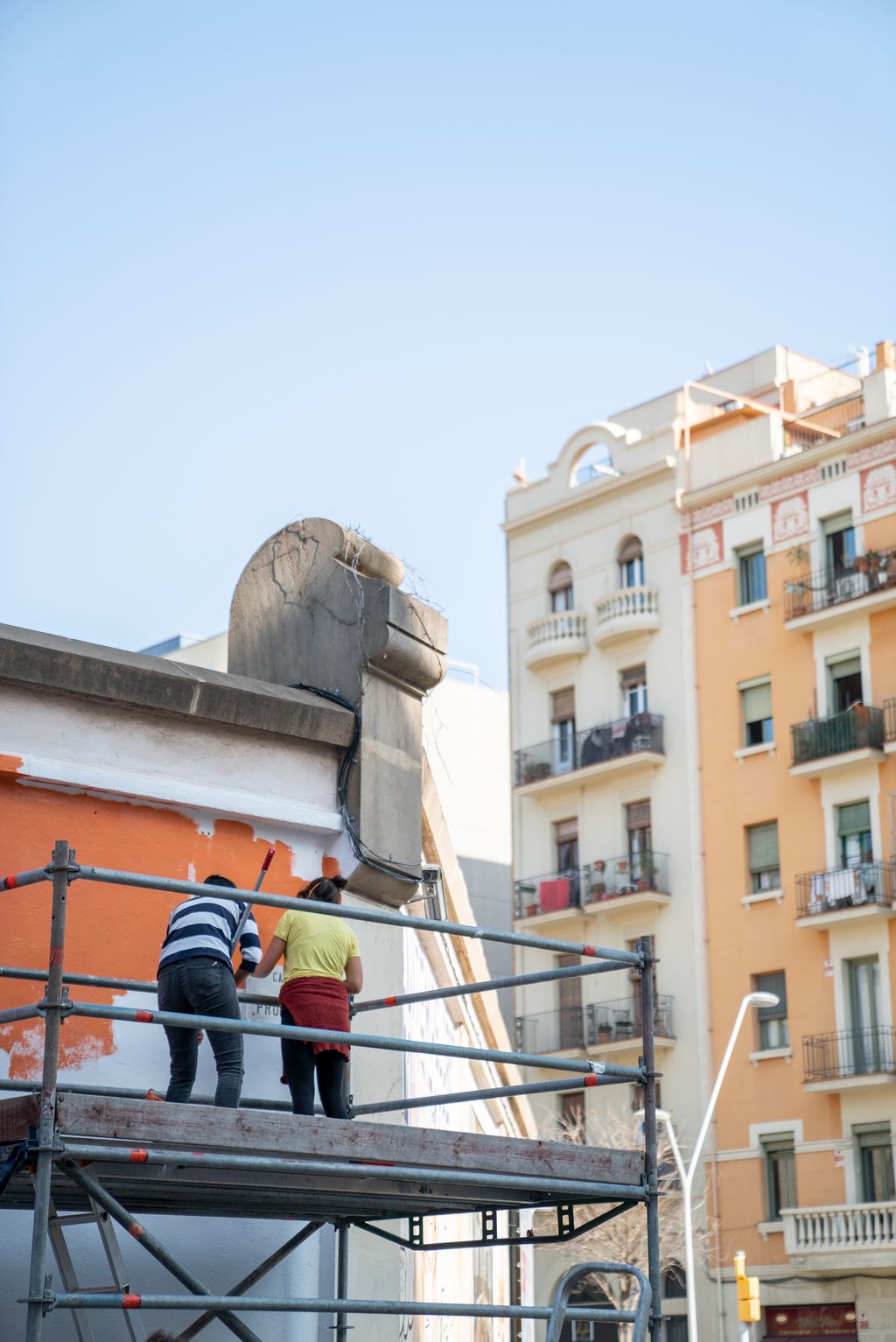 Dues il·lustradores pujades a una bastida preparant el mur perimetral de la Model per fer un mural reivindicatiu feminista