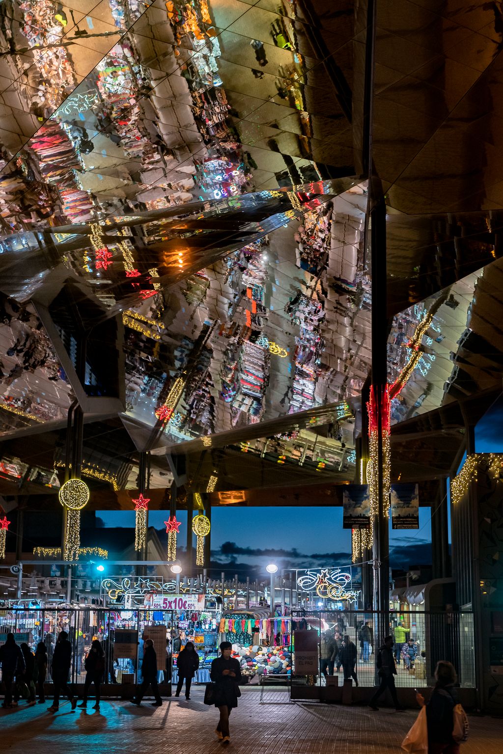Gent entrant i sortint del Mercat dels Encants il·luminat amb els llums de Nadal