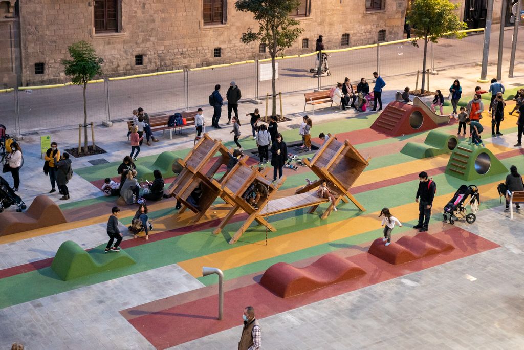 Vista de la plaça de Sant Miquel amb zones verdes i espai on es pot jugar. Hi ha moltes famílies jugant i veïns passejant