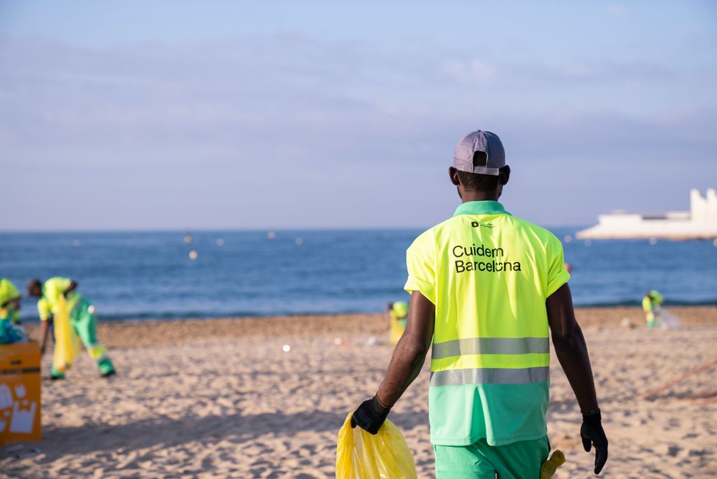 Un trabajador del servicio de limpieza camina por la playa con una bolsa para la recogida de los envases que ha dejado la gente en la arena durante la verbena de San Juan