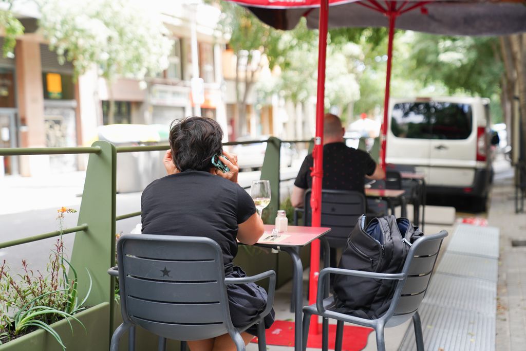 Clients asseguts i consumint una beguda en un dels nous prototips de terrasses en línia de Barcelona, que conté unes barreres metàl·liques amb jardineres