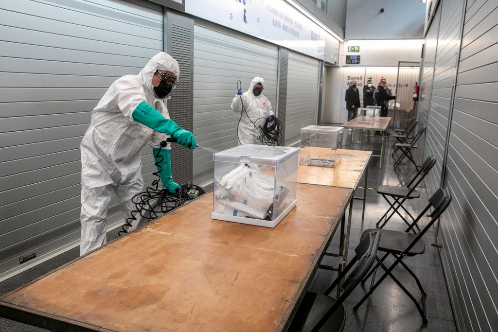 Membres de l'equip de neteja i desinfecció ruixen amb un líquid les taules, urnes i cadires que formen part del dispositiu electoral del Mercat de Sant Antoni